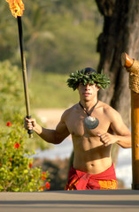 A male hula dancer runs with a tiki torch to light the stages lights for the performance.