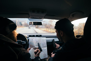 Criminals sitting at sunset in a car, looking at the city map and planning their next move.