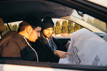 Two robbers planning and pointing on the blueprint(map) their objective while holding their guns.