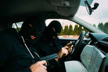 Bank robbers with their masks on pointing at the map prepared for robbing the bank,sitting in the...