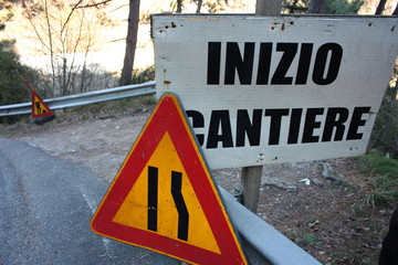 editorial photo of a road construction site. warning signs of work in progress. cartels written in Italian. public message