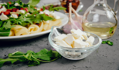 Dish with Arugula on a white plate. Green, fresh arugula on a plate, with white cheese and pasta on a stone countertop. The concept of preparing a fresh and healthy salad. Caring for health.