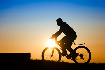 Silhouette of a young man riding a bicycle at sunset