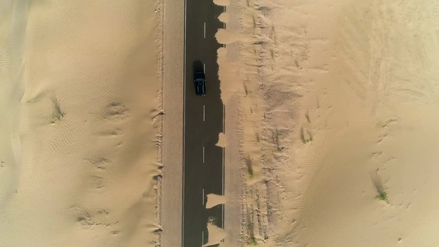 Aerial view above of black car driving on road covered by sand, U.A.E.