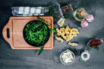 Obraz na płótnie Canvas A table when preparing a meal. Green arugula in a black bowl, feta cheese, dried tomatoes for preparing a rocket salad. The concept of preparing meals.