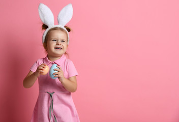 Laughting happy baby girl with painted eggs wear bunny ears on Easter day