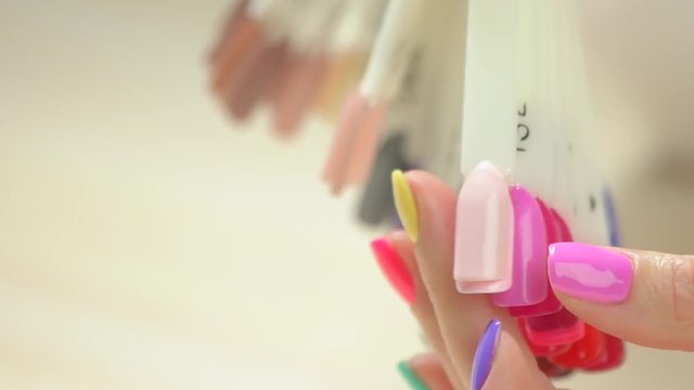 Close up artificial nail color samples. Slow motion female hand choosing nail color on collection of artificial nail samples.