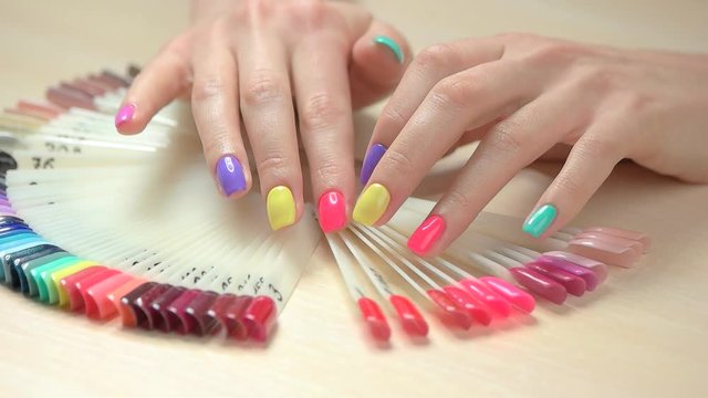 Manicured hands and nail color samples. Slow motion young woman hands with multicolored summer manicure choosing nail color on table in beauty salon.