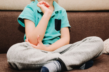 Pain in the elbow, hands of a small child. The little boy is holding his elbow, sitting on the bed....