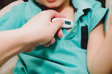 The child measures the fever with an electronic thermometer. Medicine and health concept. The thermometer held in your hand indicates a fever. Illness in a child, flu, cold.