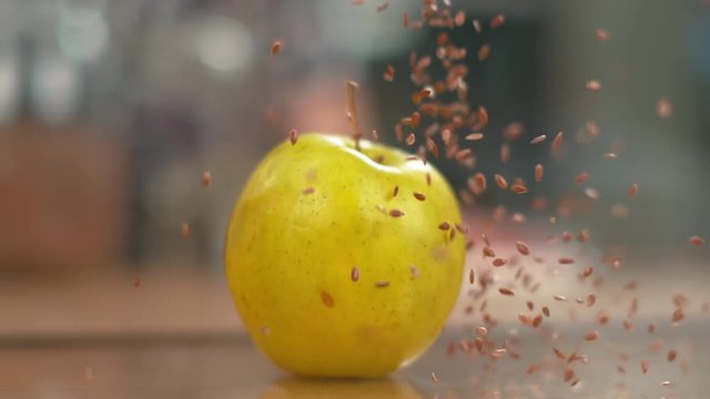 SLOW MOTION, MACRO, DOF: Tiny brown flax seeds fall from the air and onto the yellow apple set on kitchen counter. Cinematic slow motion shot of linseeds raining onto the ripe golden delicious apple.