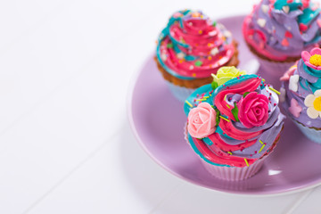 Closeup few cupcakes with creamy multicolored top decorated with colorful flowers on round plate.