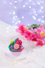 Closeup cupcake with creamy multicolored top decorated with colorful roses with pink tulips, bokeh lights and satin ribbon on blurred background.
