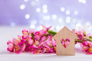 Closeup wooden house with hole in form of heart with tender pink cherry flowers on blurred lilac background with bokeh.