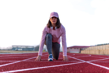 Pretty young girl doing sports on running tracks with pink cap and sweatshirt