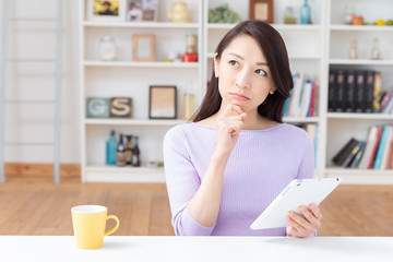 部屋でタブレットコンピューターを見る女性　考える