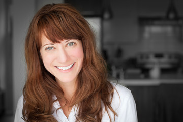 Portrait Of A Mature woman smiling At The Camera. In the kitchen.