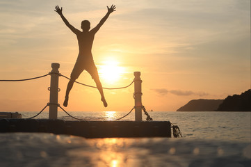Asian man jumping on floating pier at sunrise , Silhouette body of asian people early morning on the beach by the sea.