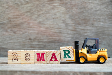 Toy forklift hold block R to complete word 29mar on wood background (Concept for calendar date 29 in month March)