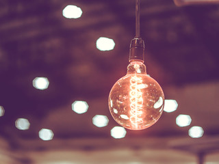 Tungsten orange light bulb hanging on the inside of the building with a black iron fence around,Lighting in buildings with multi-colored electric lamps,soft focus.Vintage colors picture,soft focus.