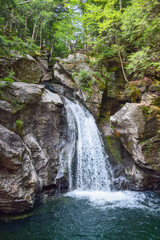 Waterfall rushing over rocks in lush green Vermont forest with swimming hole