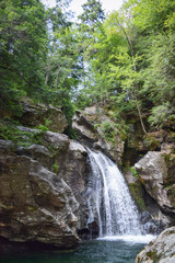 Fototapeta na wymiar Waterfall rushing over rocks in lush green forest New England landscape