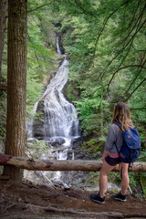 Hiker with backpack overlooking waterfall in lush green forest