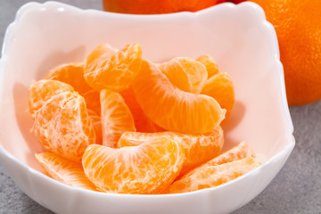 Several whole and peeled ripe tangerines on a white plate on gray background