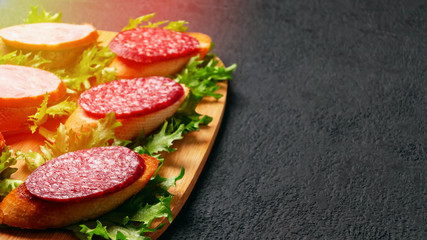 Several sandwiches with sausage and salami and sauce on a black board, background with copyspace
