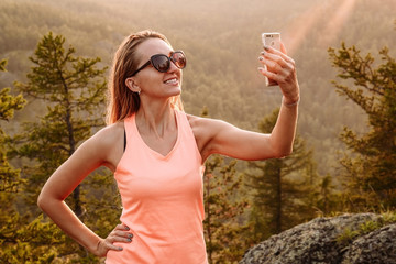 a young smiling woman makes selfi on smartphone in the mountains in summer