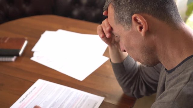 Unhappy sad man reading letter, bill, bank statement paper or tax document