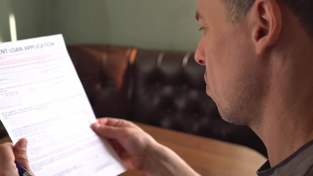 Mature man reading credit application form on a paper sheet
