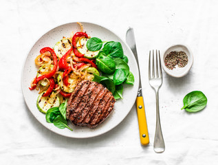 Beef steak with grilled  vegetables, sweet pepper, zucchini and fresh spinach on a light background, top view. Delicious healthy balanced lunch