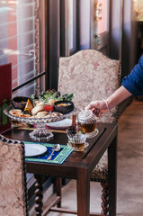 English afternoon tea with scone and puff pastries, pouring tea into tea cup