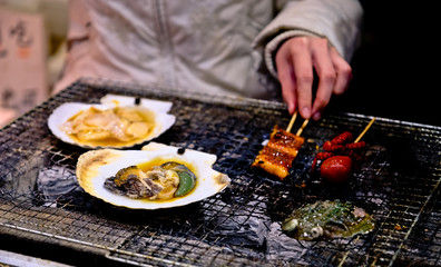 grilled abalone and other seafood cooking over the barbecue grill at fish market in Japan