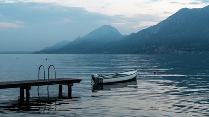 Obraz premium Beautiful landscape on lake Garda in Italy. Boat near the pier on the water surface of the water. The blue hues of the mountains.