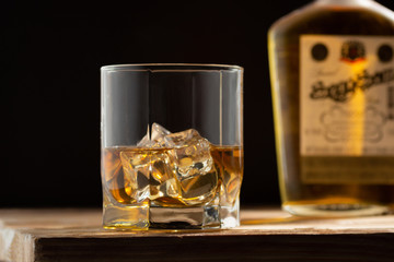 Glass of whiskey with ice cubes on a wooden table and dark background.