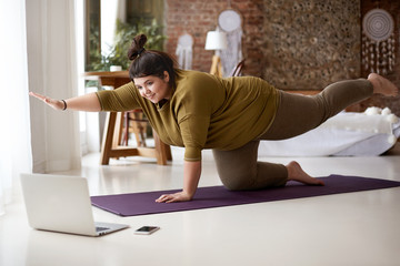 Woman doing yoga while looking at laptop