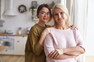 Cozy family portrait of stylish cute teenage girl in eyeglasses embracing her charming beautiful...