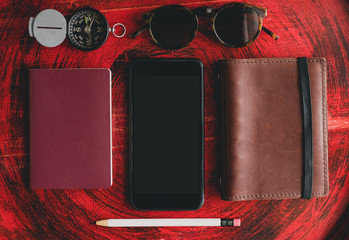 Set of mobile, passport ,notebook,sunglasses,compass and white pencil on rustic red wood round table near window.Tropical Summer Holiday vacation concept.clipping path on smartphone screen.
