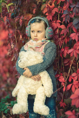 Little girl with her Teddy bear in autumn leaves