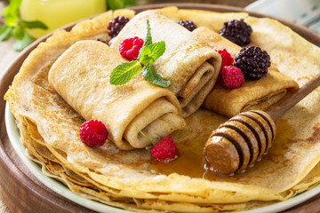 Healthy Pancakes breakfast close-up. Stack of homemade thin pancakes or crepes on a rustic table, served with honey and fresh berries.