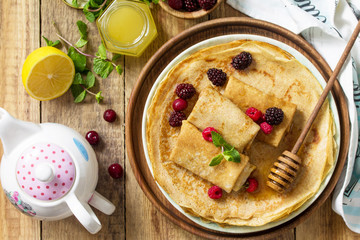 Healthy Pancakes breakfast. Stack of homemade thin pancakes or crepes on a rustic table, served with honey and fresh berries. Top view flat lay background.