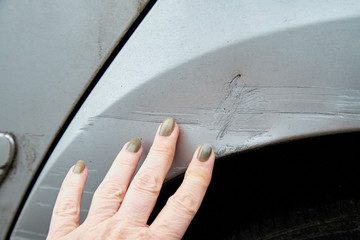 Female hand showing the scratches on the damaged car of silver color