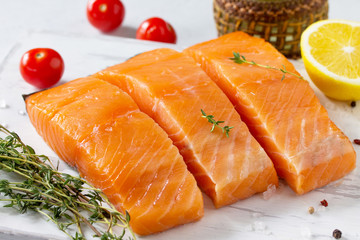 Fresh Fish. Raw Salmon Fillet, Lemon and tomatoes on a wooden board on a white stone table.