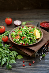 Traditional tabbouleh salad on dark brown wooden rustic background. Ingredients couscous, parsley, mint, onion, tomato. Close up view