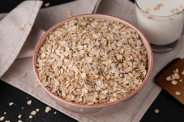 Oatmeal in a plate and a cup of milk on a towel on black background. Healthy food. close up