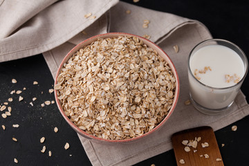  Oatmeal in a plate and a cup of milk on a towel on black background. Healthy food. close up