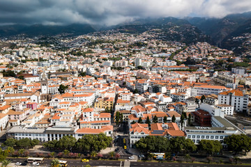 Fototapeta na wymiar Urban landscape. Panorama of the city of Funchal. View of the city from the waterfront to the top of the mountains. In the mountains-fog over the city-the sun.