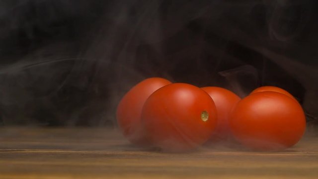 Red and fresh cherry tomatoes on a black background from which blows freshness and coolness, evaporation, close-up, copy space, slow motion